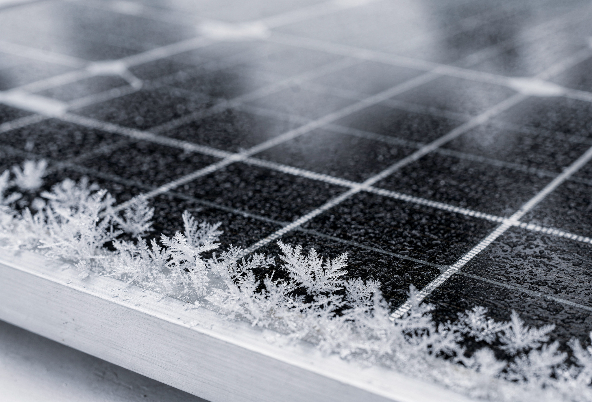Close-up of a black solar panel surface with frost crystals along its lower frame